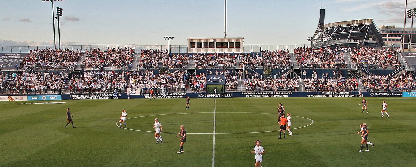 Jeffrey Field seen from behind the goal in late-afternoon light, both stands full and play underway around the centre circle