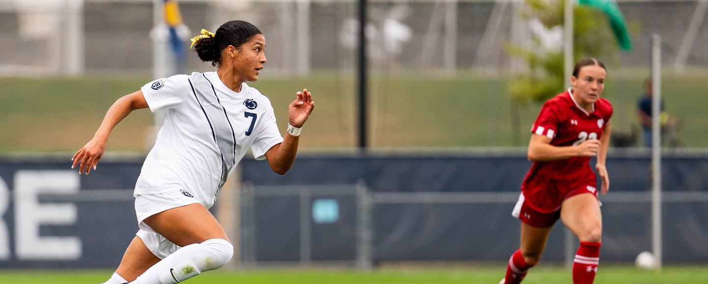 A Penn State player in the white kit at full sprint, an opponent in red a step behind, in bright daylight